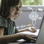 A child at a light wood desk studying a small 3D-printed toy they are deciding how to change, a tablet pushed slightly aside, a sketch notebook nearby, and a clear empty desktop space for the product.