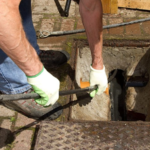 A drainage engineer carrying out urgent work at an external chamber. Image sourced from the Quick Clear Drainage website.