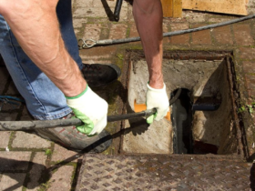 A drainage engineer carrying out urgent work at an external chamber. Image sourced from the Quick Clear Drainage website.
