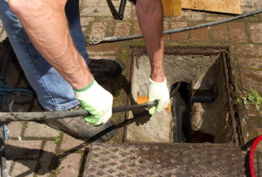 A drainage engineer carrying out urgent work at an external chamber. Image sourced from the Quick Clear Drainage website.